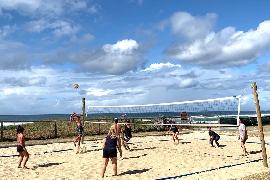A group of men and women play volleyball on the sand at a sunny beach