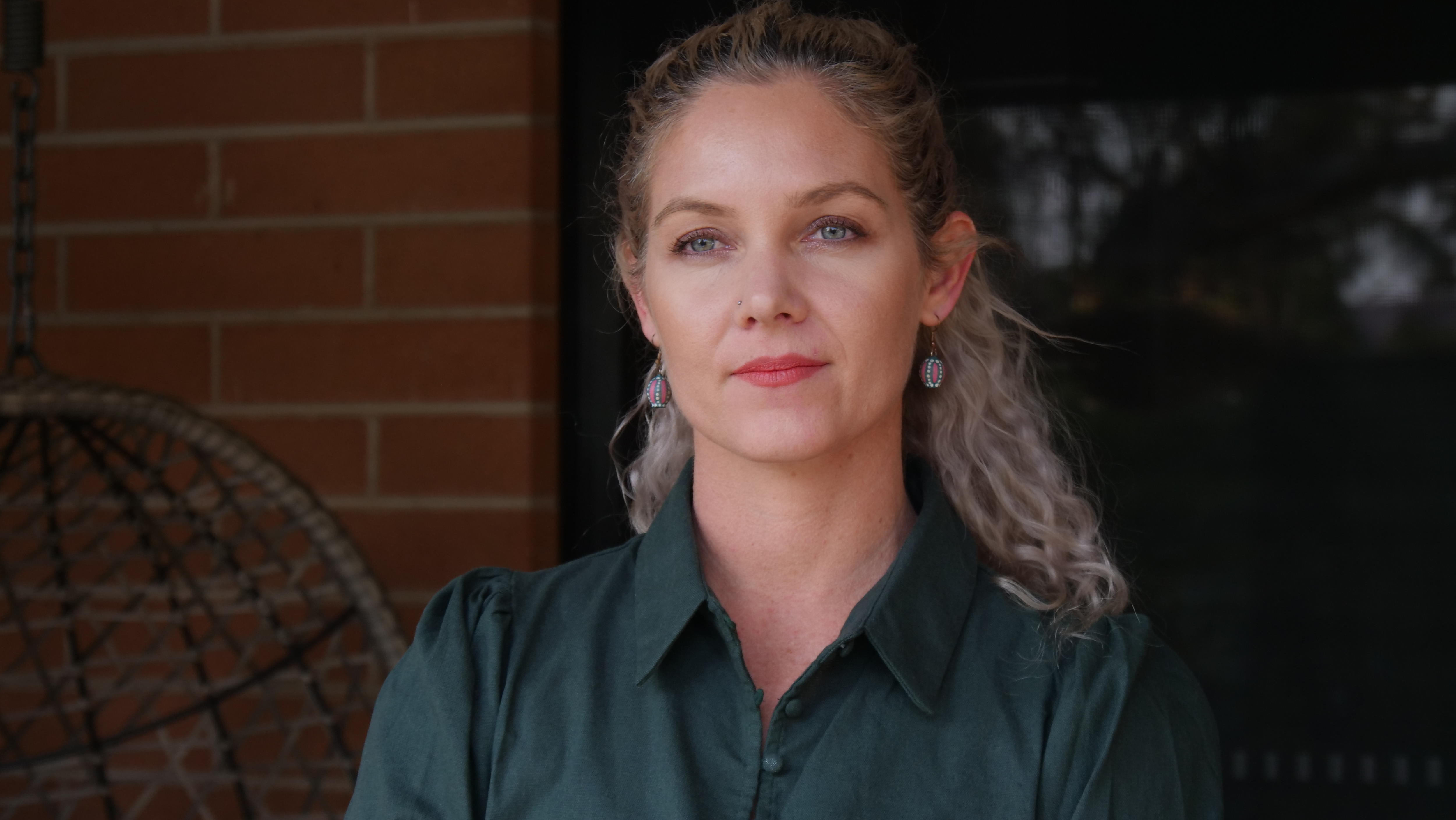 A woman standing in front of the entrance of a house, looking serious. 