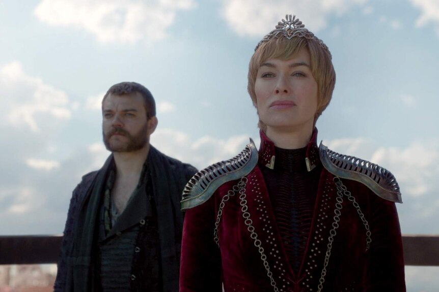 Cersei in her finery and crown looks at something off screen.