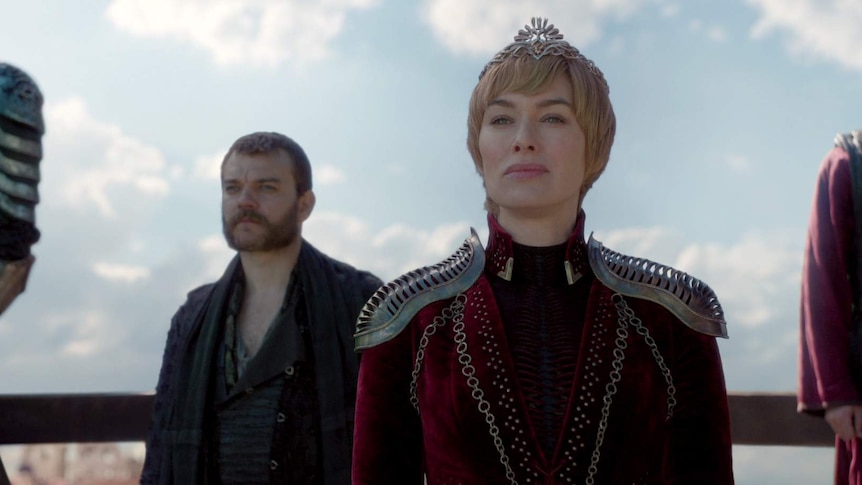 Cersei in her finery and crown looks at something off screen.