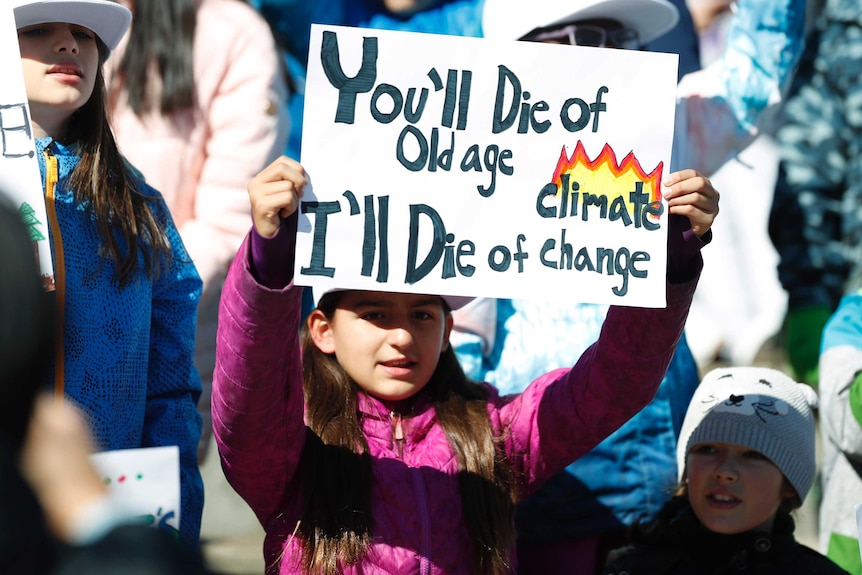 A young girl holds up a sign with the words 'you'll die of old age I'll die of climate change' on it