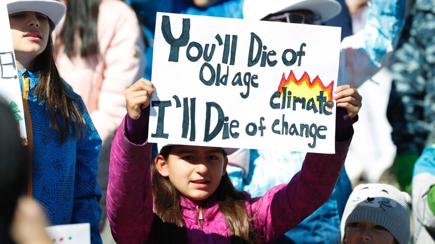 A young girl holds up a sign with the words 'you'll die of old age I'll die of climate change' on it