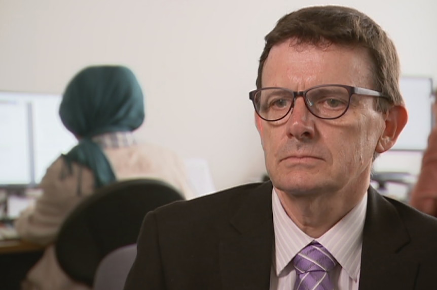 Headshot of Australian Refugee Council CEO Paul Power sits in an office.