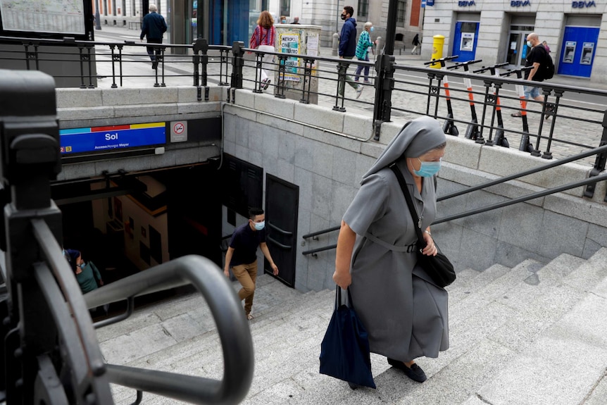 Una monja enmascarada sube los escalones de un túnel para evitar la propagación del virus corona.