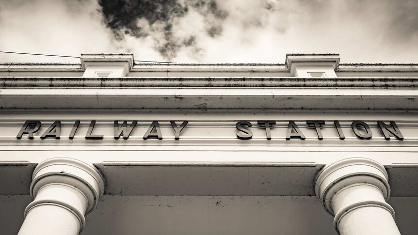 A black and white image of the entrance to a railway station from standing underneath