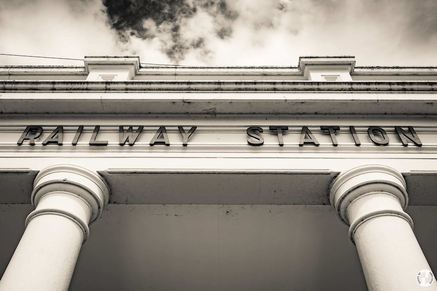 A black and white image of the entrance to a railway station from standing underneath