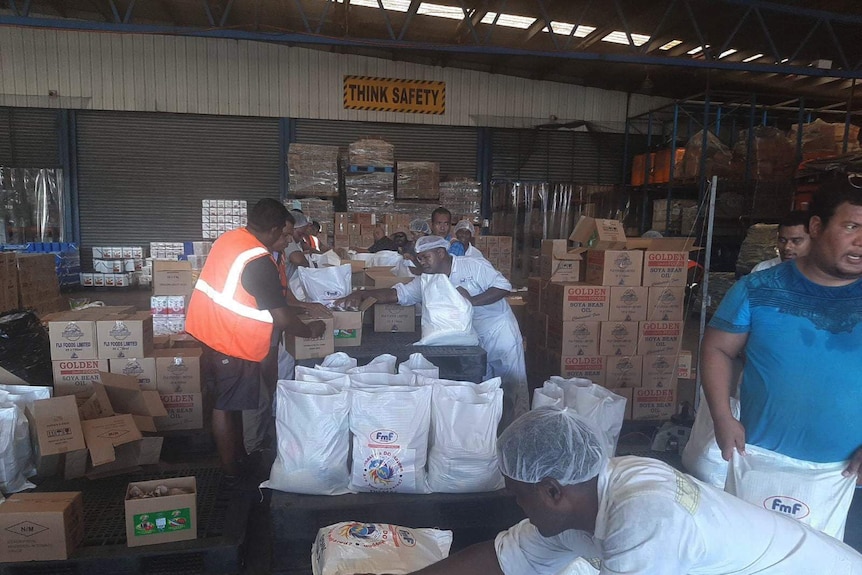 People pack supplies into boxes and bags in a warehouse in Fiji.