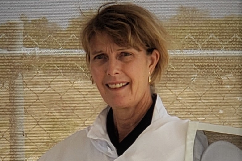A woman poses for a photo wearing a white bee keeping uniform. 