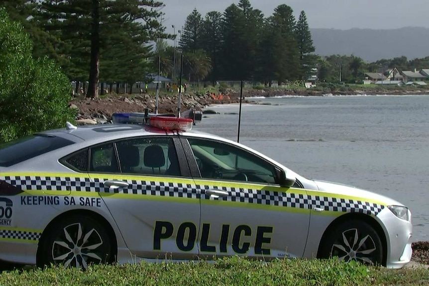 A police car in front of a rocky shore and sea