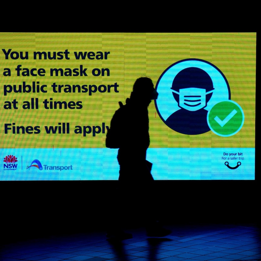 A masked pedestrian walks past a COVID safety sign at a Sydney train station.