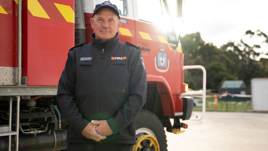 A firefighter in front of a firetruck smiles at the camera