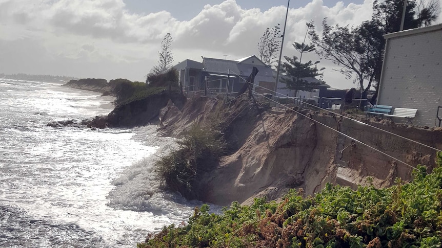 Water is lapping against the side of a major drop off at the beach, metres from buildings.