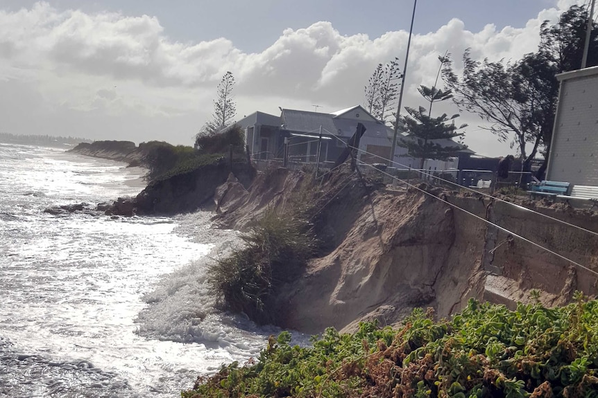 Water is lapping against the side of a major drop off at the beach, metres from buildings.