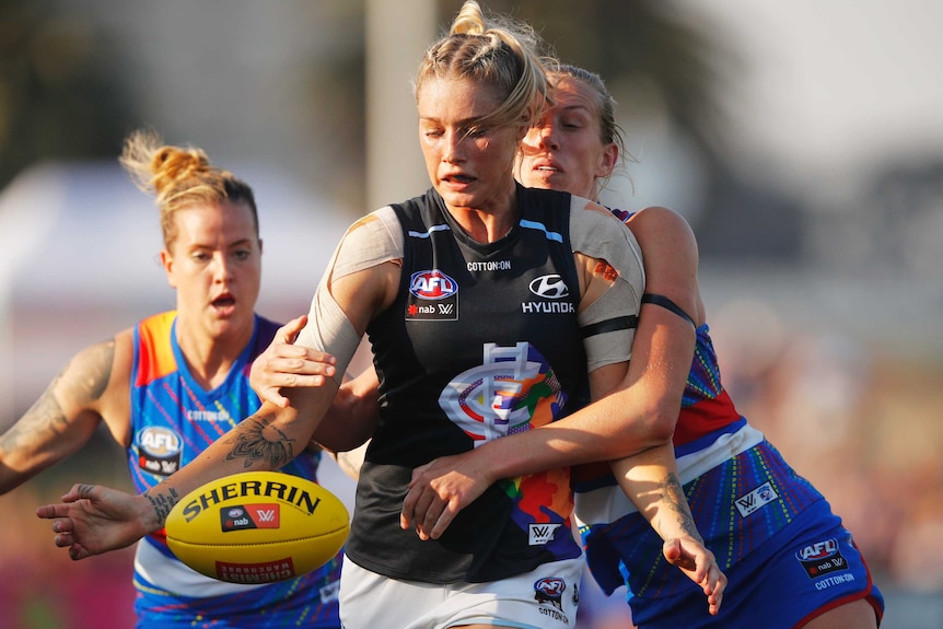 Tayla Harris looks to kick the ball away as an opponent tries to tackle her from behind