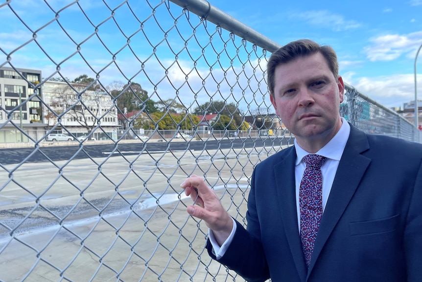 A man wearing a suit and tie next to a fence