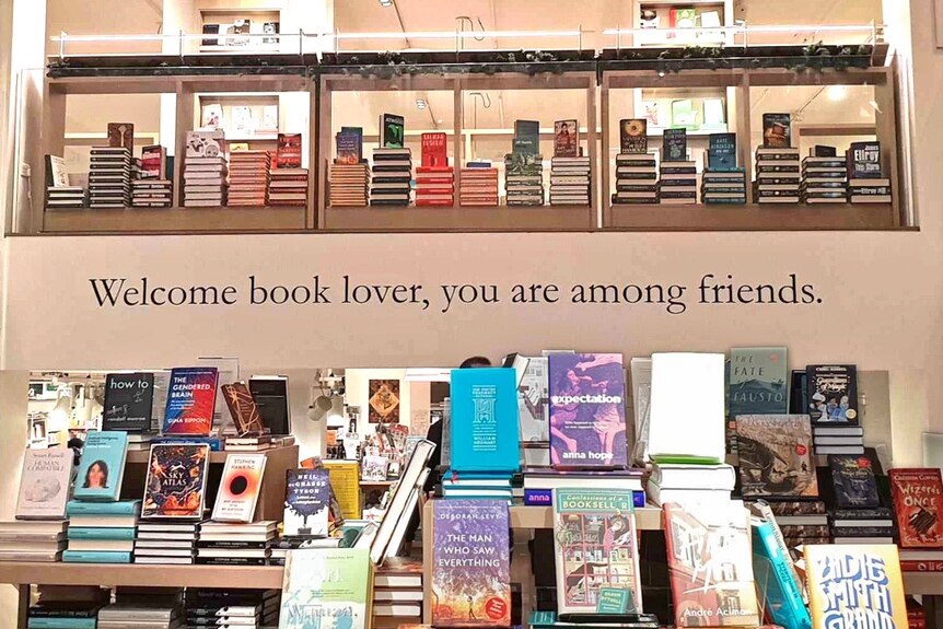 The crowded bookshelves of a bookshop. "Welcome book lovers, you are among friends" is printed on the wall.