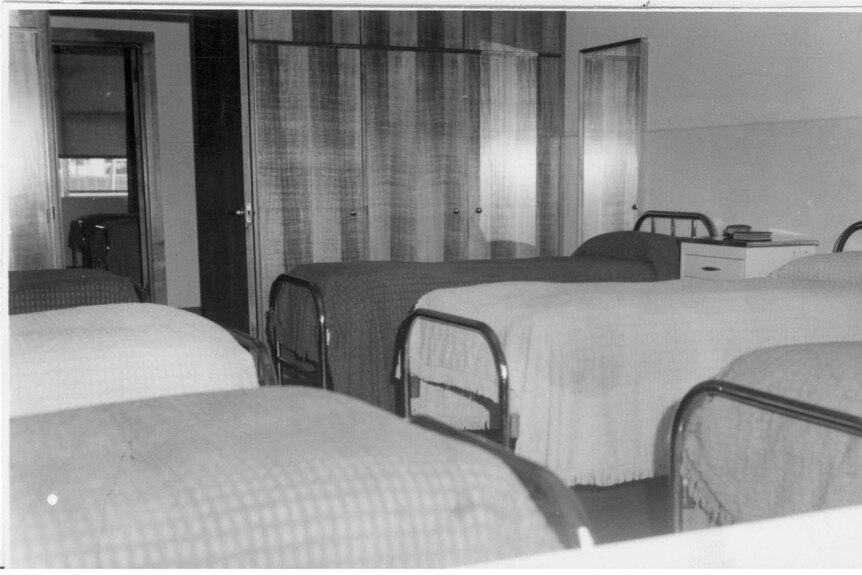 Black and white image of single beds lined up in a dormitory