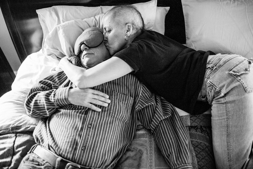 Laurel Borowick hugs leans over to hug Howie, as he sleeps on a bed.