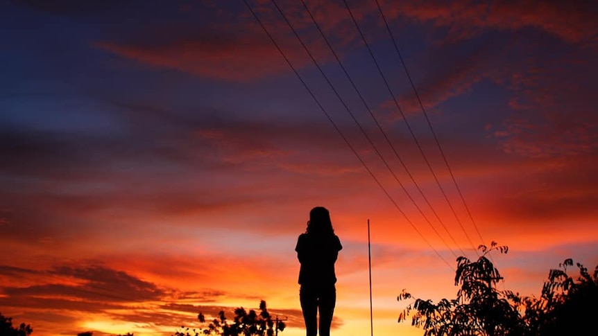 A silhouette of a woman watching a vast sunset in a remote town 