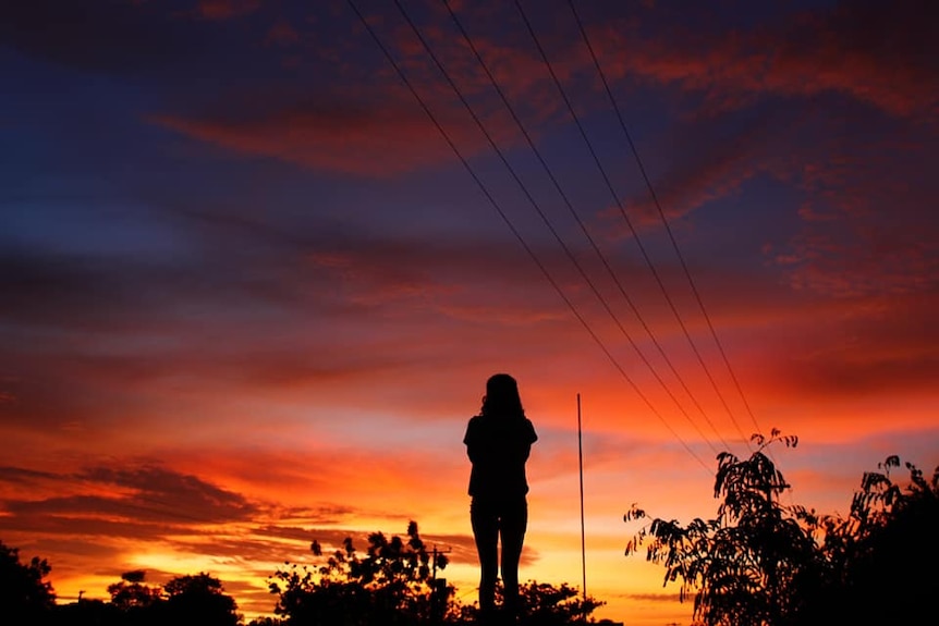 A silhouette of a woman watching a vast sunset in a remote town 