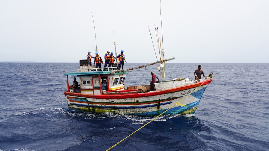 A group of people wearing life jackets stand on board a boat in the ocean.