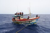 A group of people wearing life jackets stand on board a boat in the ocean.