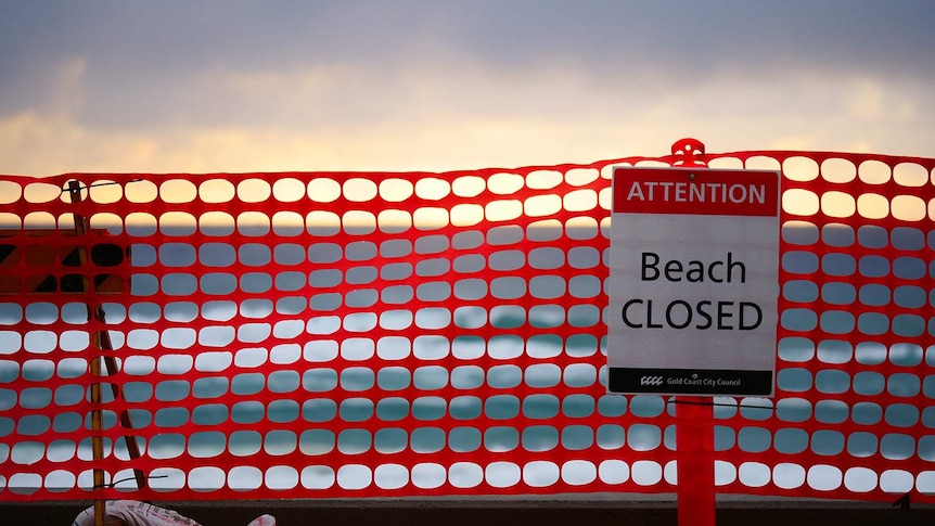 Beach in far distance with temporary fence and beach closed sign blocking access