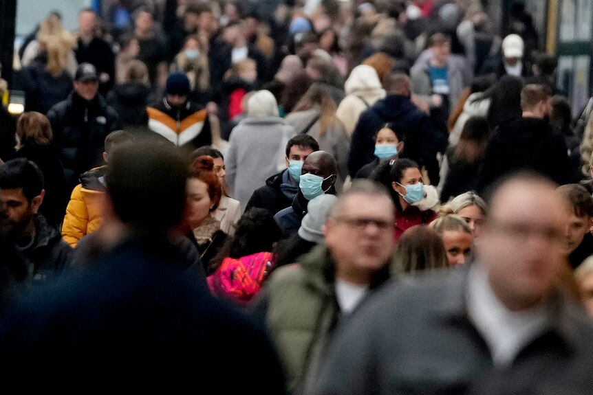 Dozens of people walk along a busy street in London, some wearing face masks