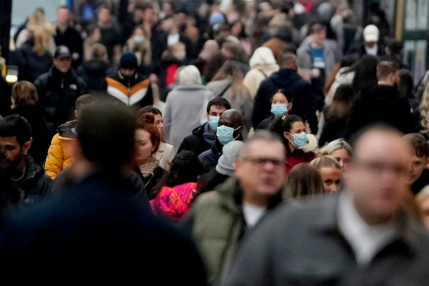 Dozens of people walk along a busy street in London, some wearing face masks