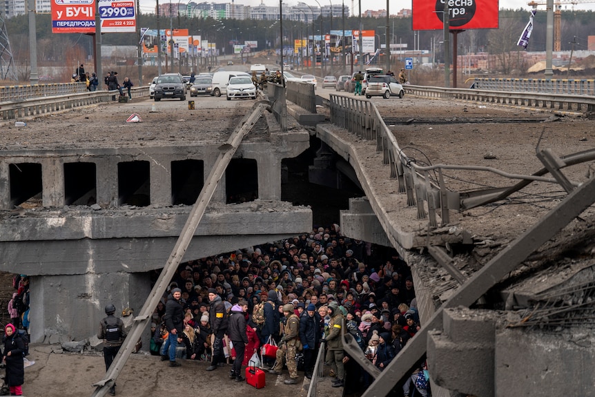 Large crowds gather under a destroyed bridge.