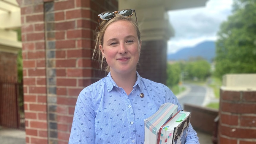 A young woman holds books outside a school