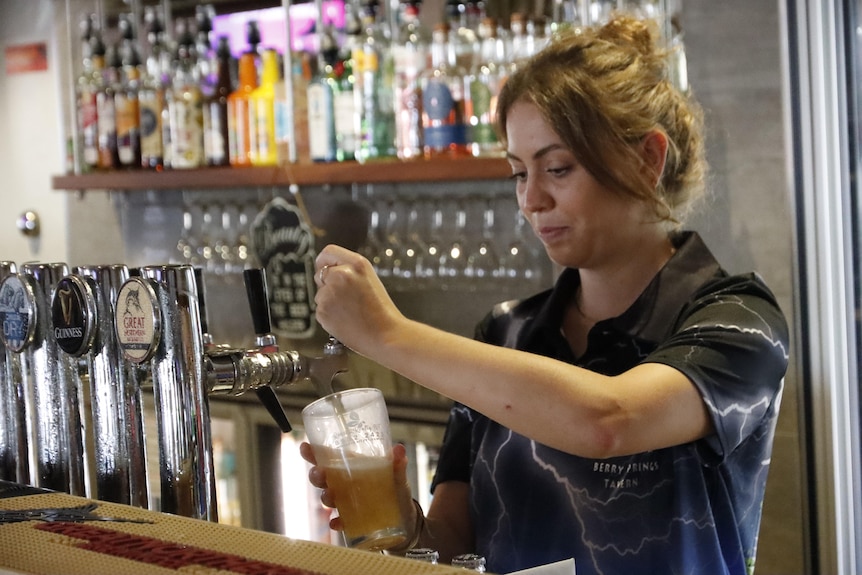 A woman behind the bar of an outback tavern pours a beer