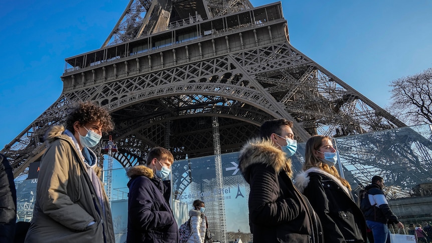 People wearing face masks walk past Paris's Eiffel Tower
