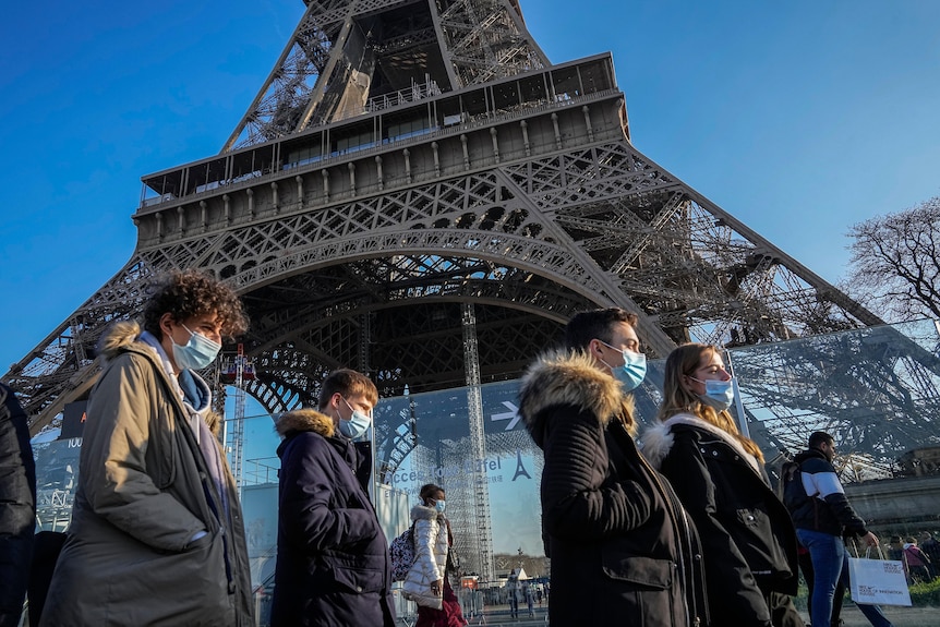 People wearing face masks walk past Paris's Eiffel Tower