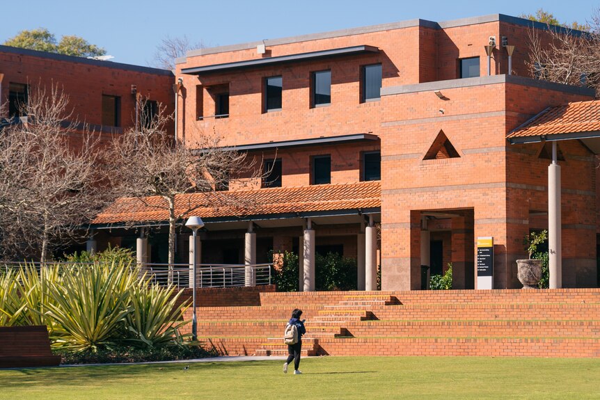 A photo of an orange building at Curtin University with lawn in front and one person walking along it.