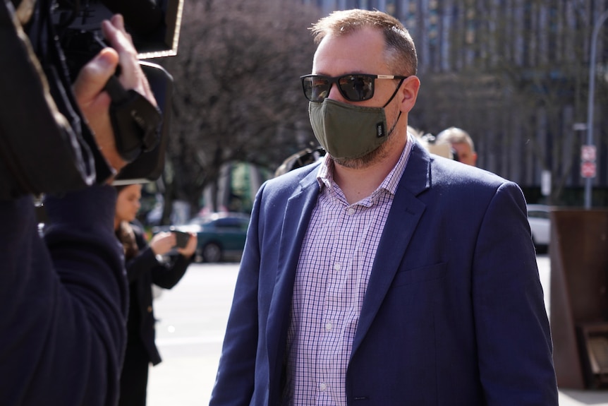 A man wearing sunglasses and a face mask walks outdoors
