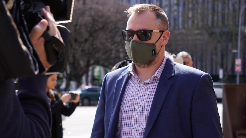 A man wearing sunglasses and a face mask walks outdoors