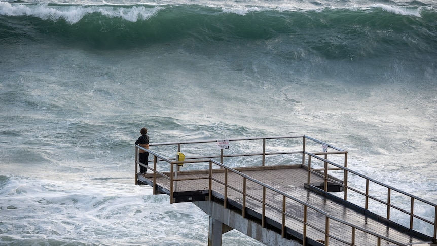 A person stands at an ocean lookout in front of large swell and a wave.