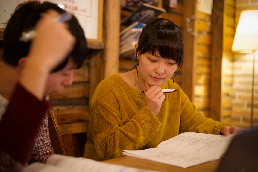 Two students read textbooks together while sitting inside.