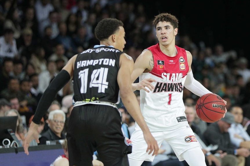 An NBL player holds the ball while sizing up the play as a defender guards him.