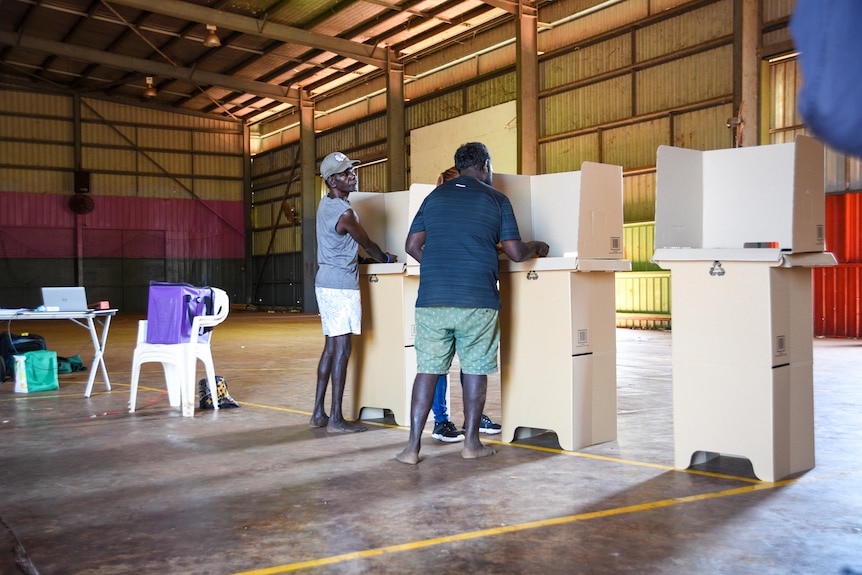 Two Aboriginal men stand at temporary voting booths inside a hall