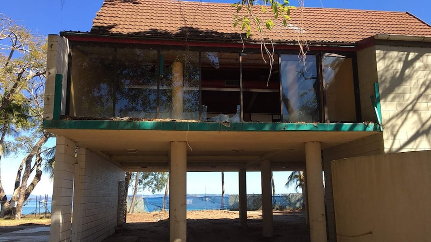An old and abandoned building with smashed glass windows on a beach.