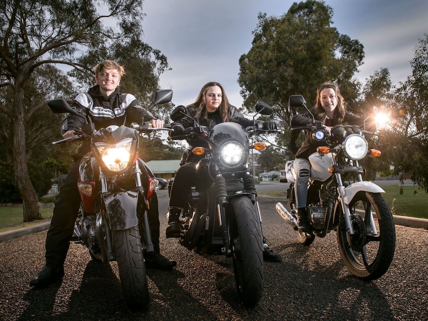 Three young people sitting on motorbikes with headlights pointing towards camera