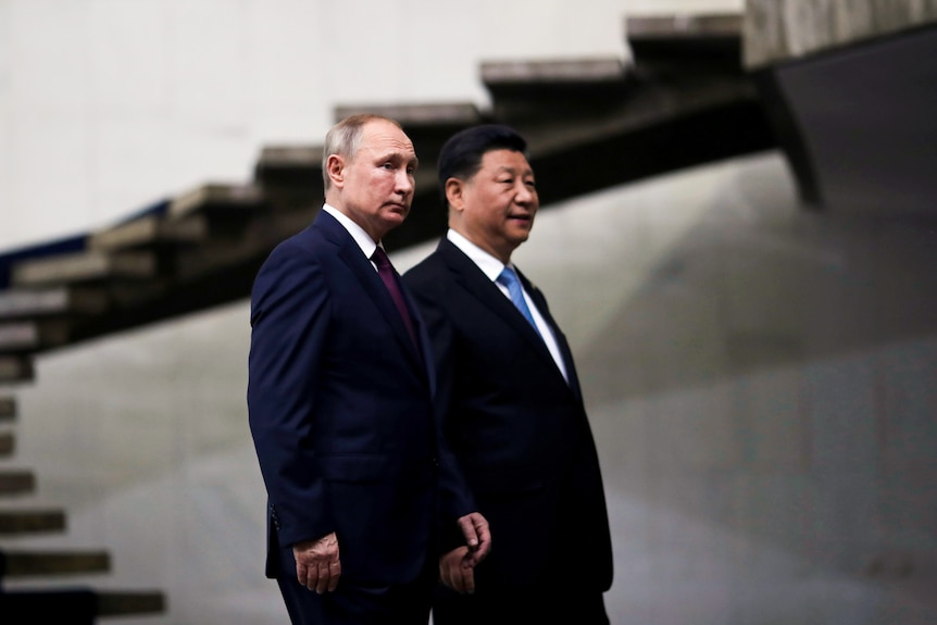 Vladimir Putin wearing a suit walks next to Xi Jinping in a suit.