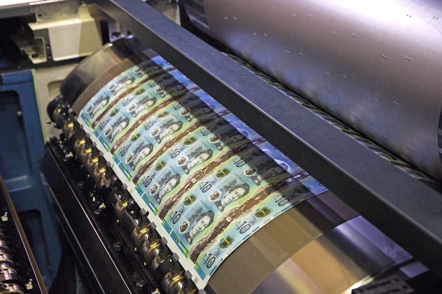 A feed of 10 dollar notes moves through a press, wound around a reel.
