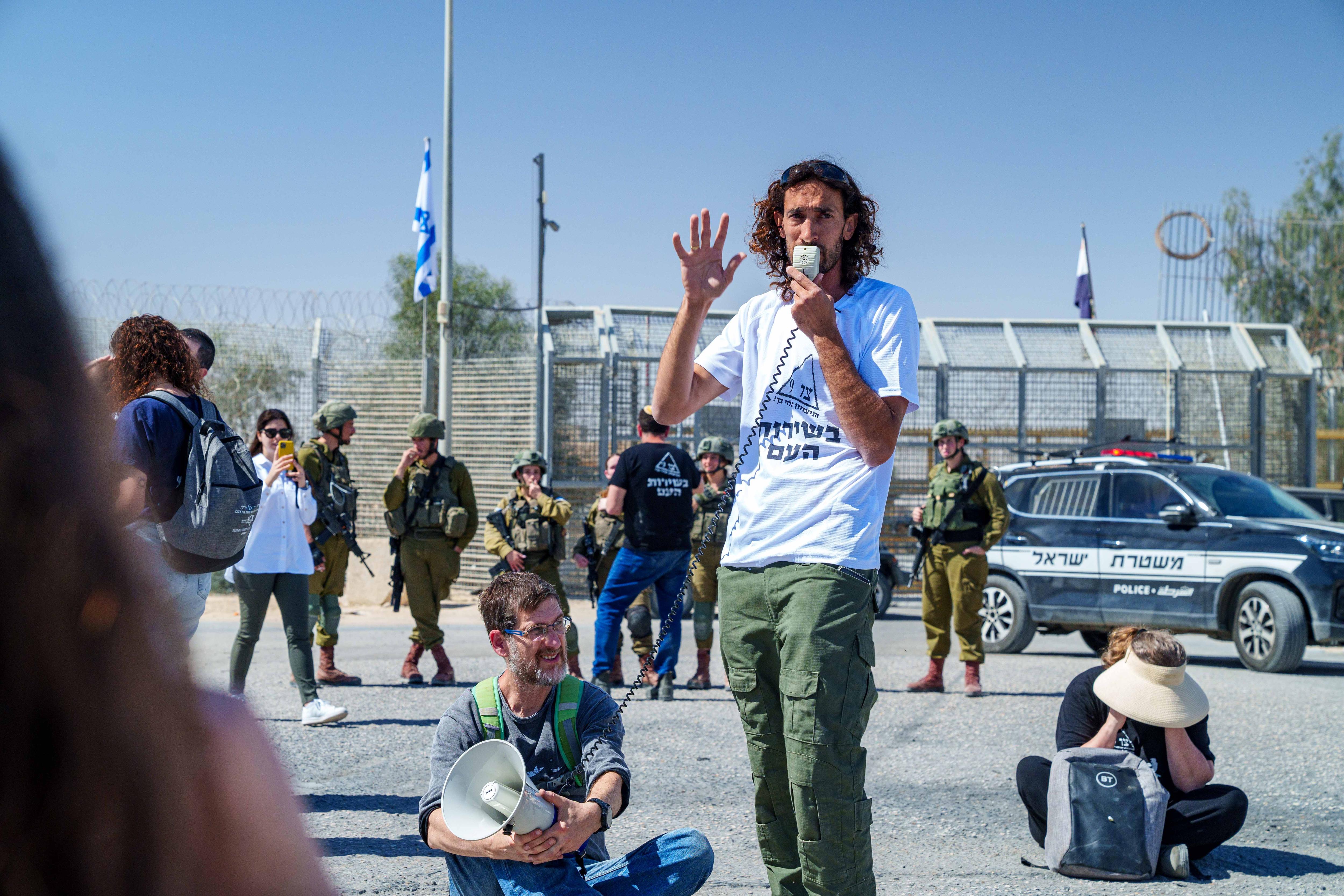 A man in a white t-shirt talks into a microphone 
