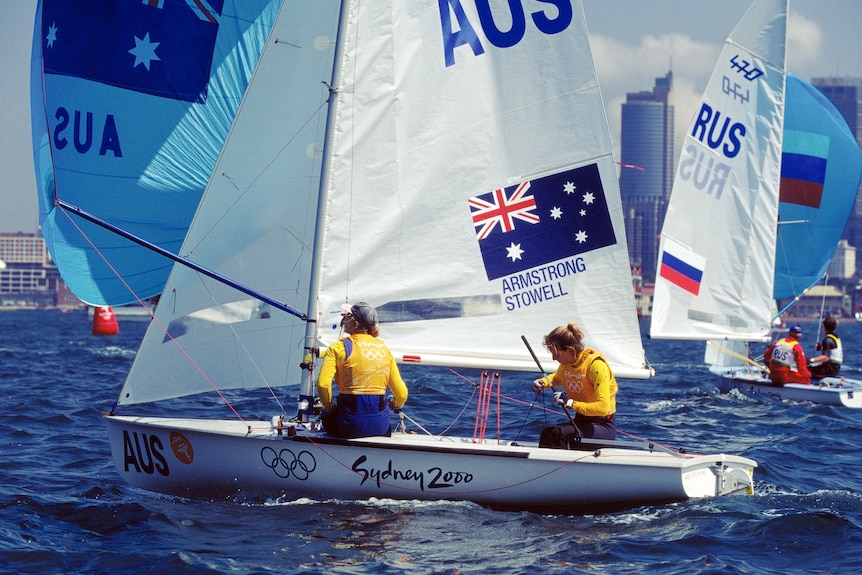 Two women sit on a competitive sailing boat on Sydney Harbour.