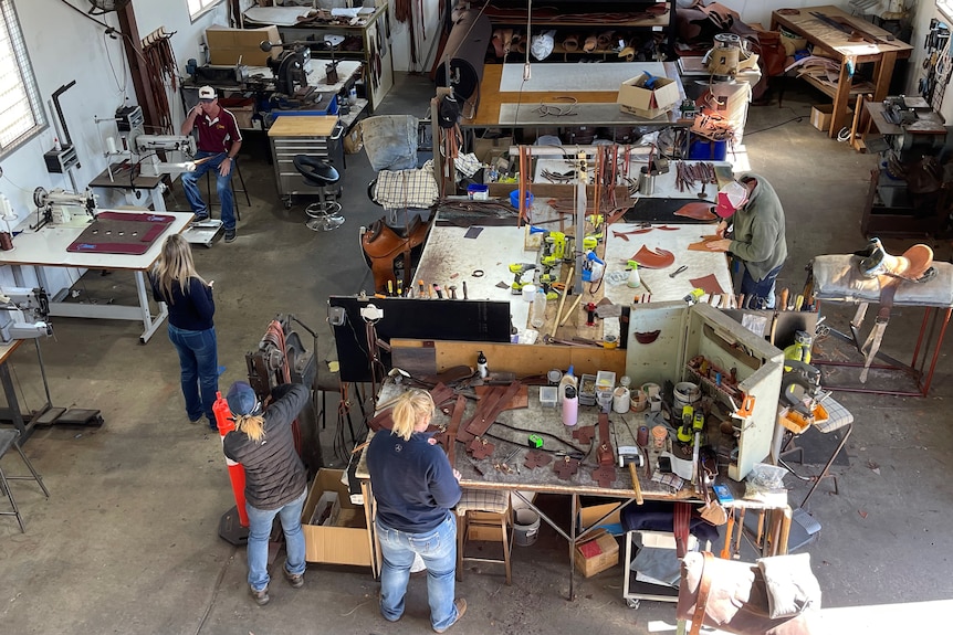 A birds eye view of a workshop where three women and two men are working on leather products.