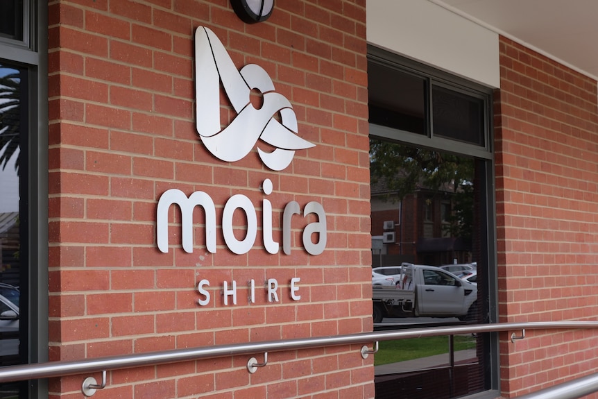 A silver logo says 'moira shire', stuck on a red brick wall.