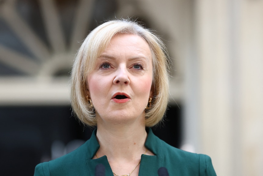 close up of liz truss speaking, wearing a green suit, ion front of the door of number 10
